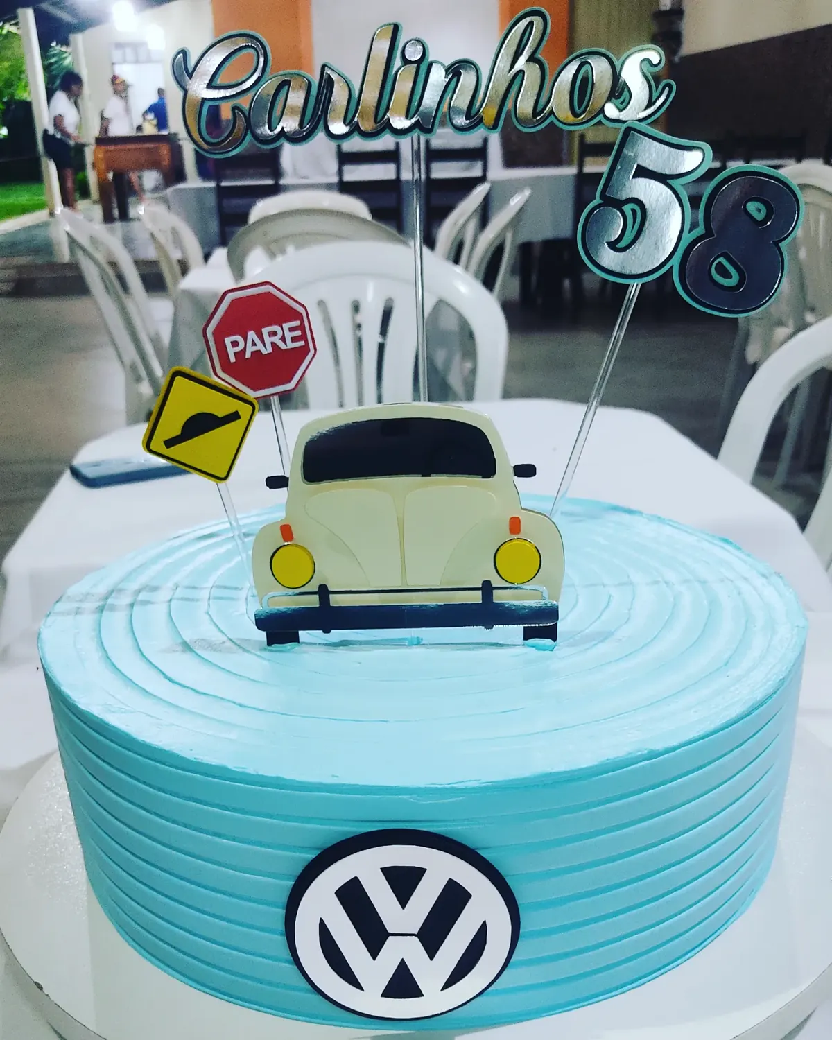 Bolo azul com topo de fusquinha, placa de pare e o nome Carlinhos 58
